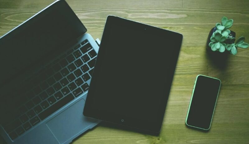 Laptop, tablet, and phone on a desk.