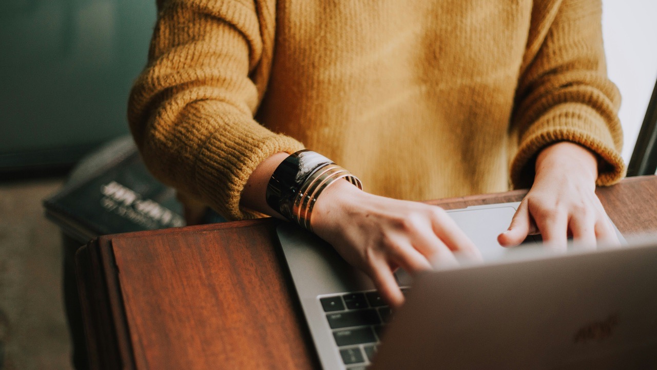 An image of a woman in a yellow sweater typing on her computer